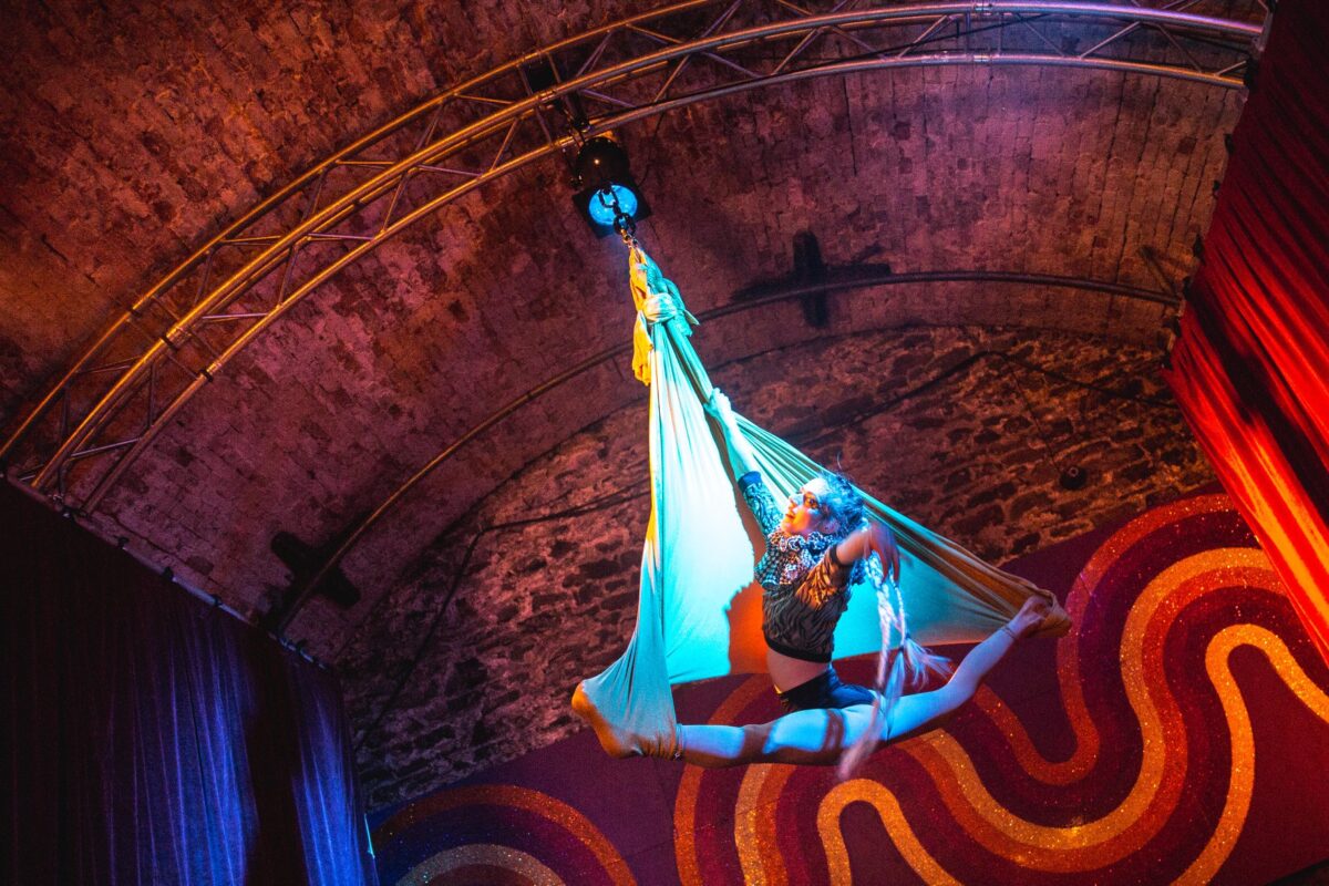 Arial performer hanging from ceiling of tunnel in splits
