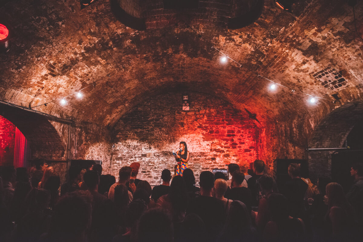 Spoken word artist sat on centre stage with crowd looking on