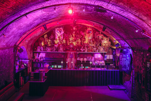 A a head on photo of the bar at Loco Klub. The bar is being lit up by a pink light.
